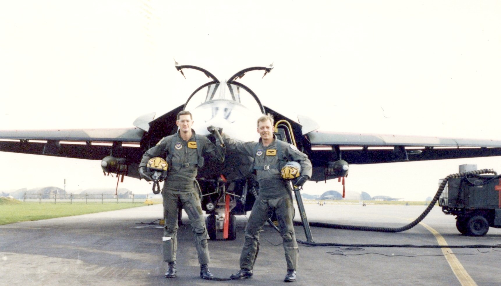 Two aircrew standing with helmets beneath the open canopy of the F-111